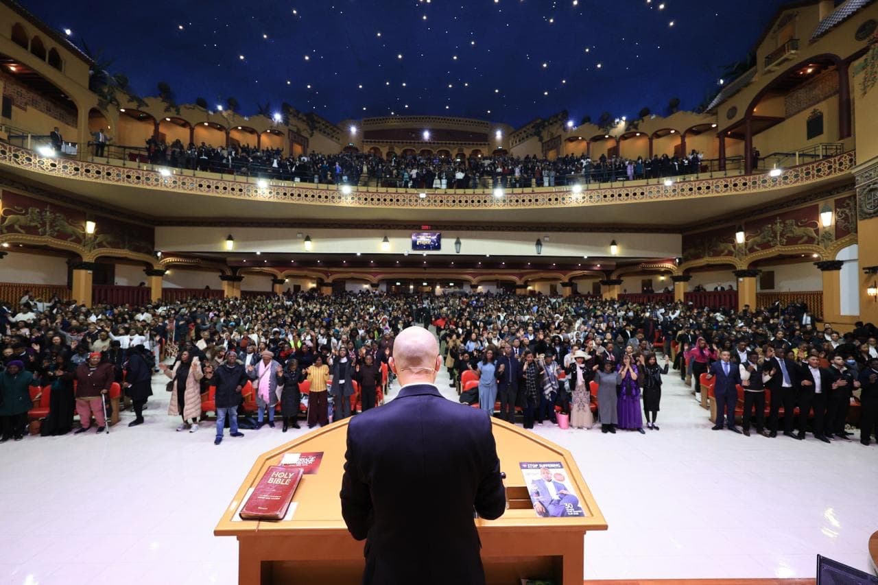 A packed Universal Church service at the Rainbow Theatre with the congregation standing in prayer